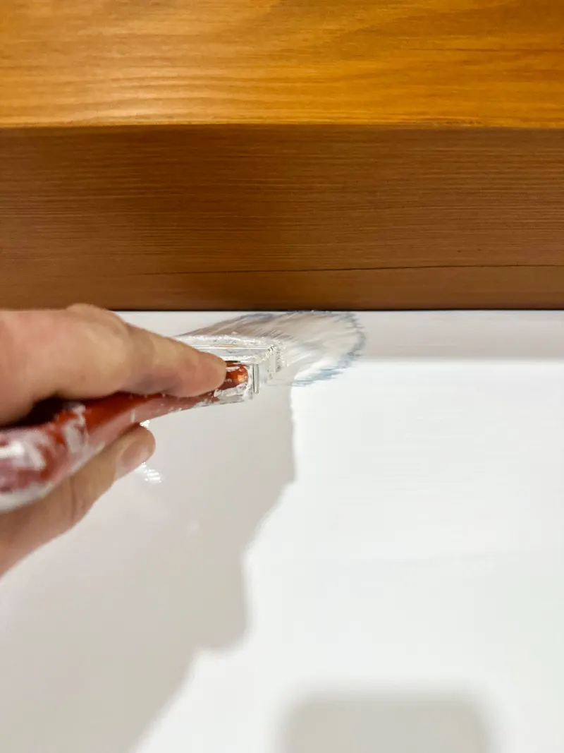Close-up of a brush cutting a clean white line against a stained wood beam