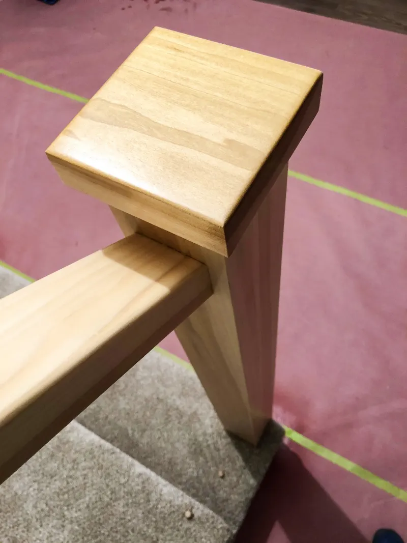 Wood newel post and handrail being finished, with the stairs masked off