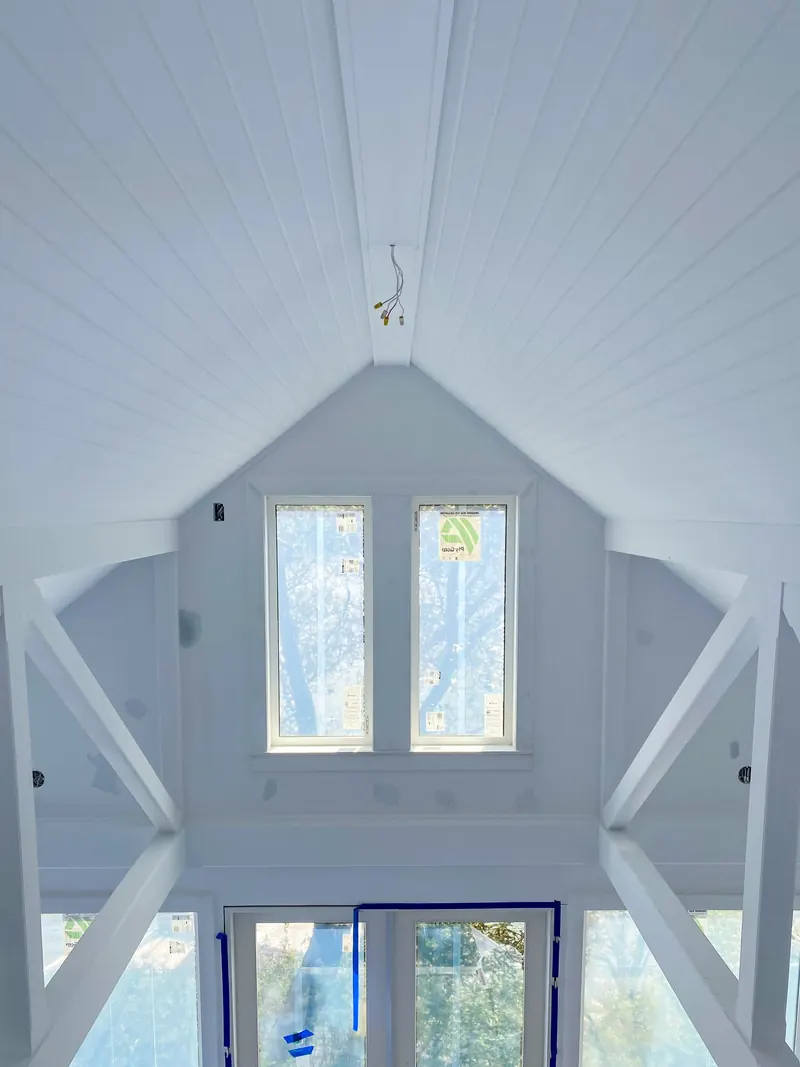 Vaulted white plank ceiling and trusses over a tall gable window, freshly painted