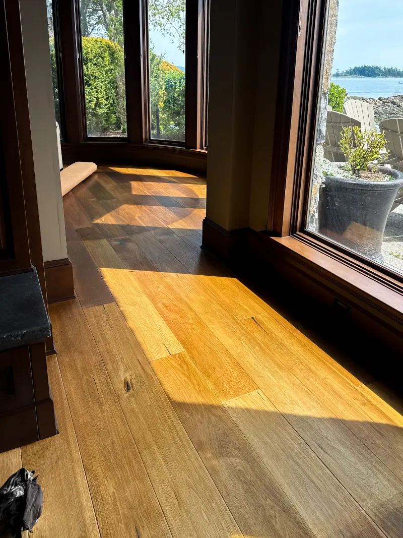 Rich stained window casings and warm hardwood floor in sunlight, with the ocean outside