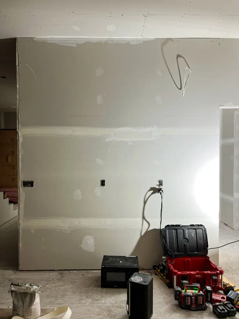 Drywall wall with taped and mudded seams and tools on the floor