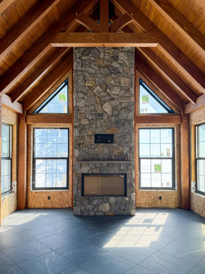 Timber-frame room with stained beams, trusses and plank ceiling around a stone fireplace
