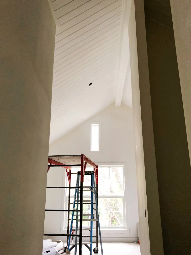 Tall vaulted white plank ceiling with scaffold and ladder below